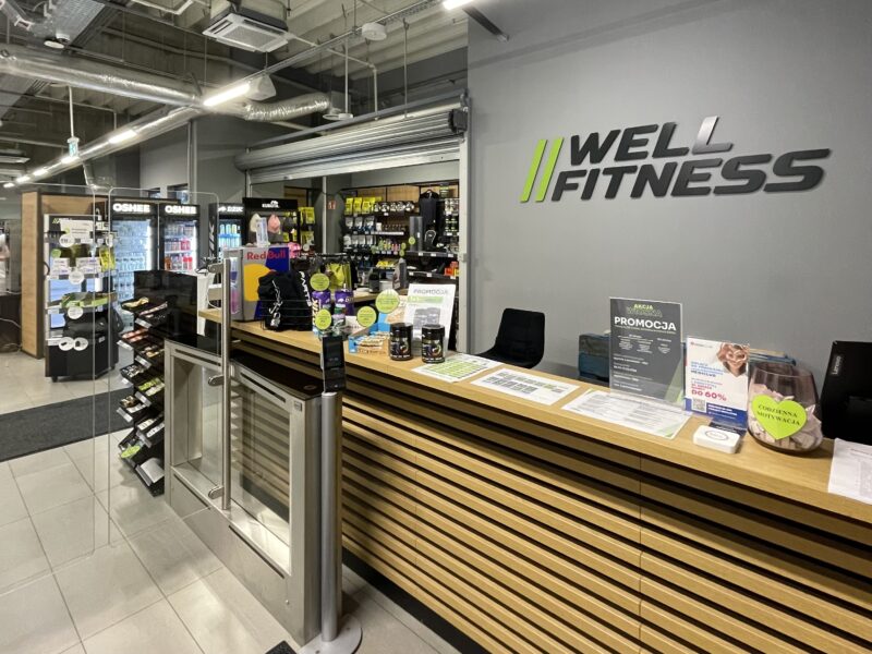 Рецепція тренажерного залу Well Fitness у Вроцлаві, в районі Карловіце, з акційною пропозицією та напоями.