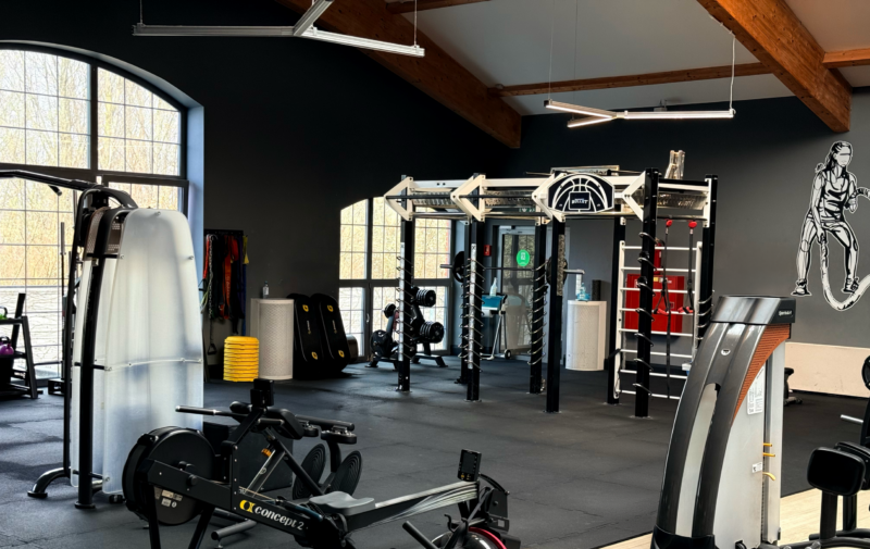 Інтер'єр функціональної зони тренажерного залу Well Fitness у Вроцлаві з гребним тренажером, кліткою для функціональних тренувань та тренувальними килимками.
