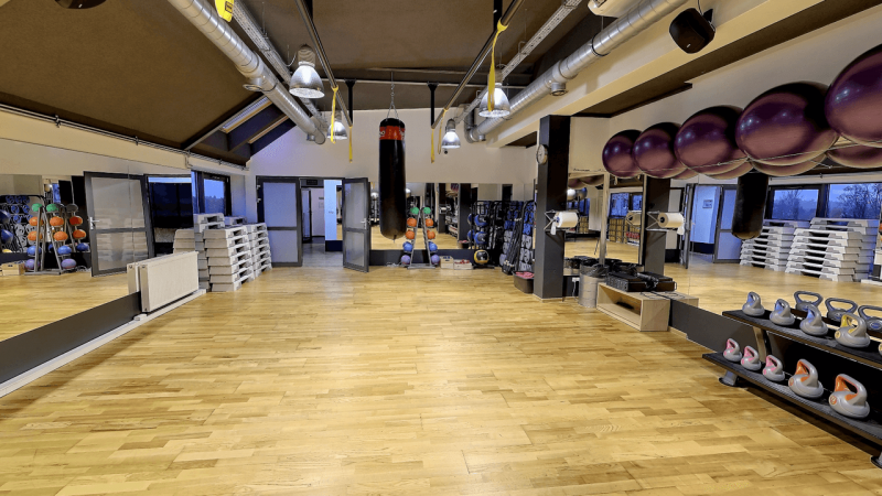 Sala fitness do zajęć grupowych z akcesoriami do ćwiczeń, lustrami, piłkami oraz workami treningowymi.