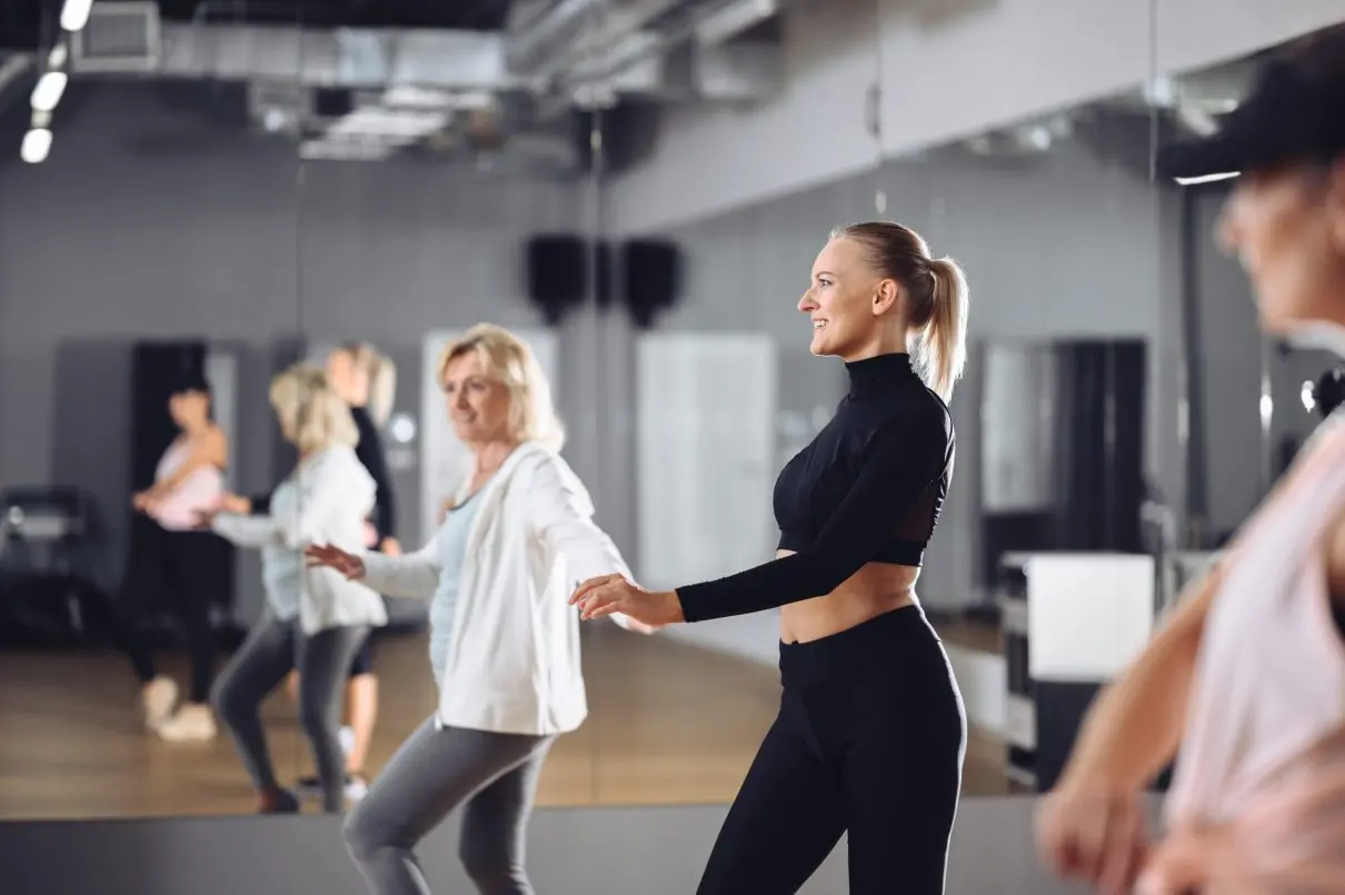Grupa kobiet podczas zajęć tanecznych w Well Fitness, ćwiczących przed lustrem w sali fitness