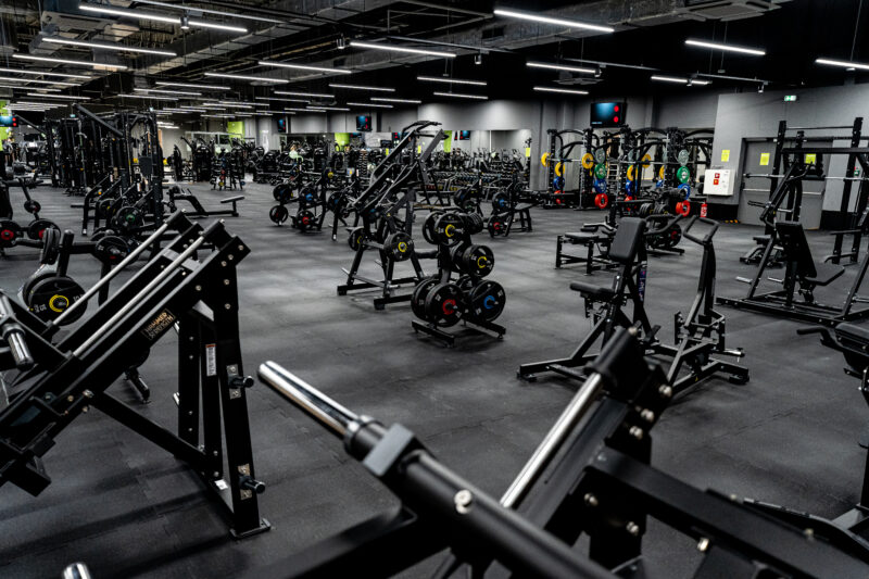 Widok na strefę treningu siłowego z maszynami typu Hammer Strength i talerzami olimpijskimi w Well Fitness.