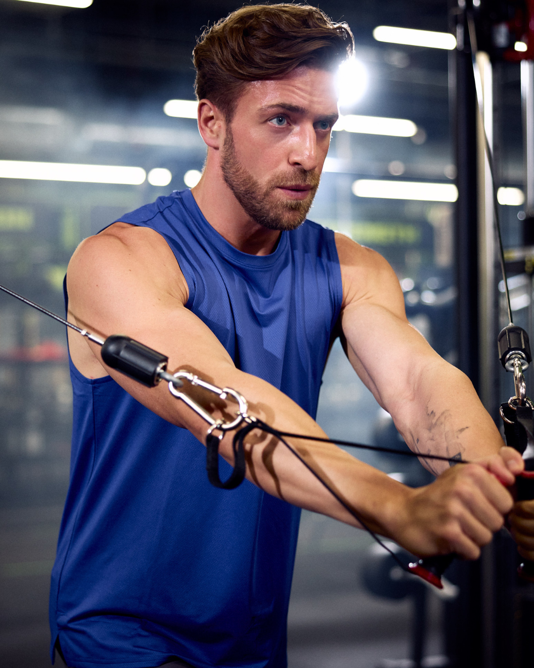 Mężczyzna trenujący na bramie z wyciągami w nowoczesnej siłowni Well Fitness, wykonujący rozpiętki na klatkę piersiową.