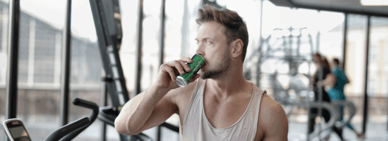 Mężczyzna pijący shot przedtreningowy na siłowni przed rozpoczęciem treningu