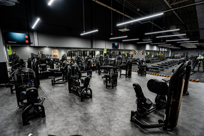 Przestronna strefa maszyn izotonicznych do treningu siłowego w nowoczesnym wnętrzu siłowni Well Fitness.