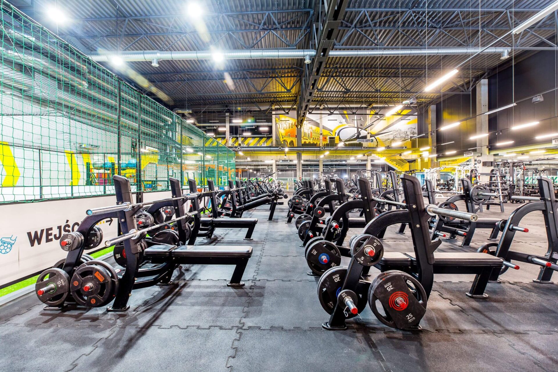 Przestronna strefa wolnych ciężarów i treningu siłowego w Well Fitness Aleja Pokoju XXL w Krakowie z licznymi stanowiskami do wyciskania i hantlami.