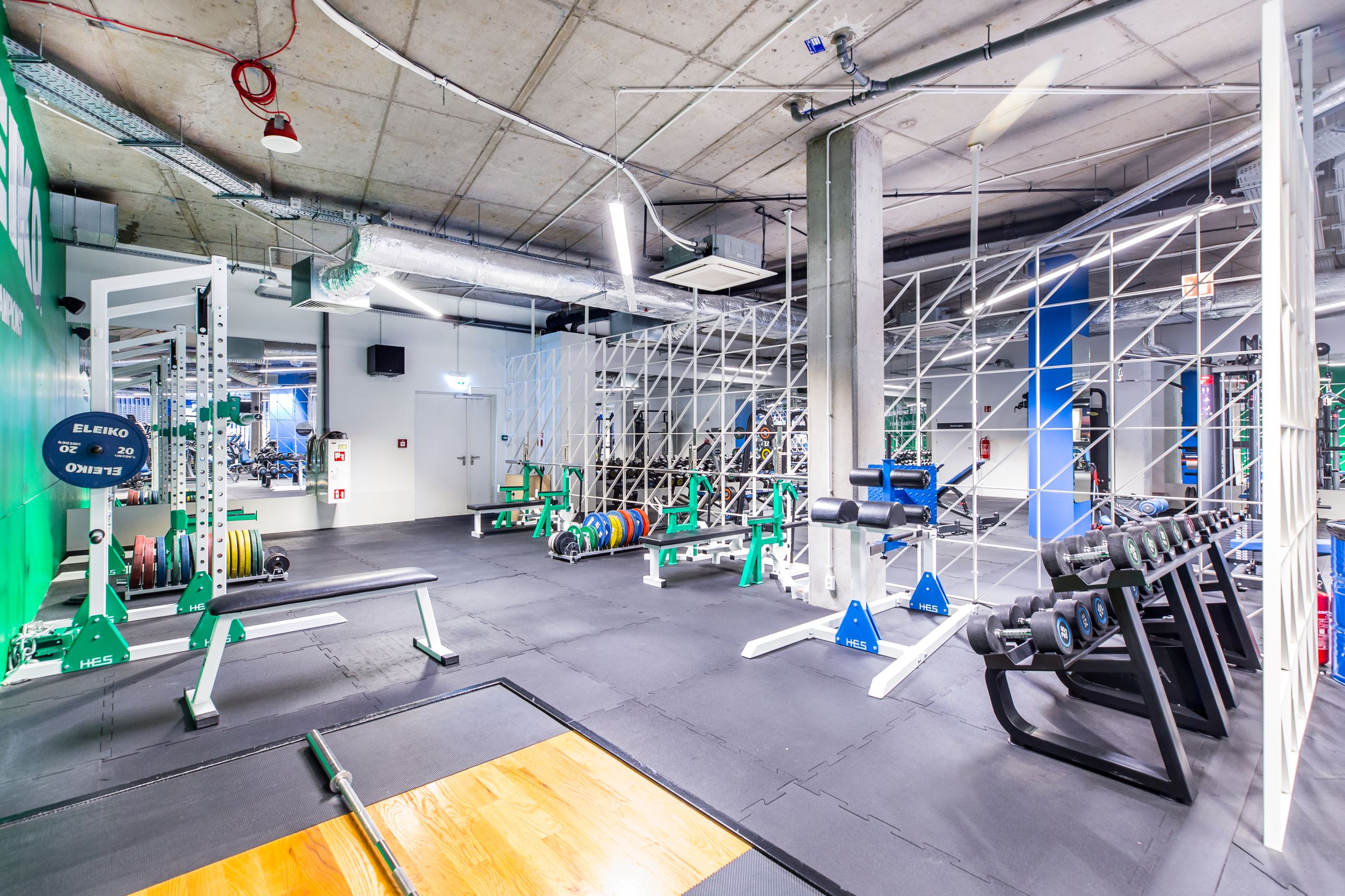 Industrialna strefa trójboju i treningu siłowego w Well Fitness Klimeckiego w Krakowie z profesjonalnymi pomostami, obciążeniami Eleiko i klatkami.