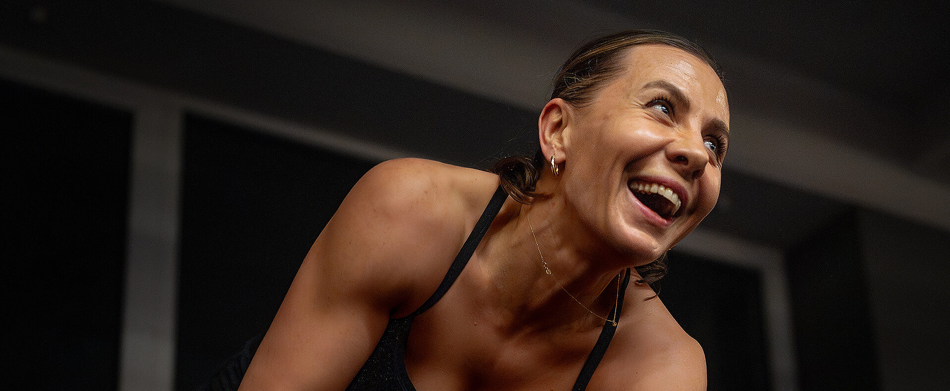 Uśmiechnięta kobieta w sportowym stroju podczas treningu w klubie fitness, patrząca z radością w bok.