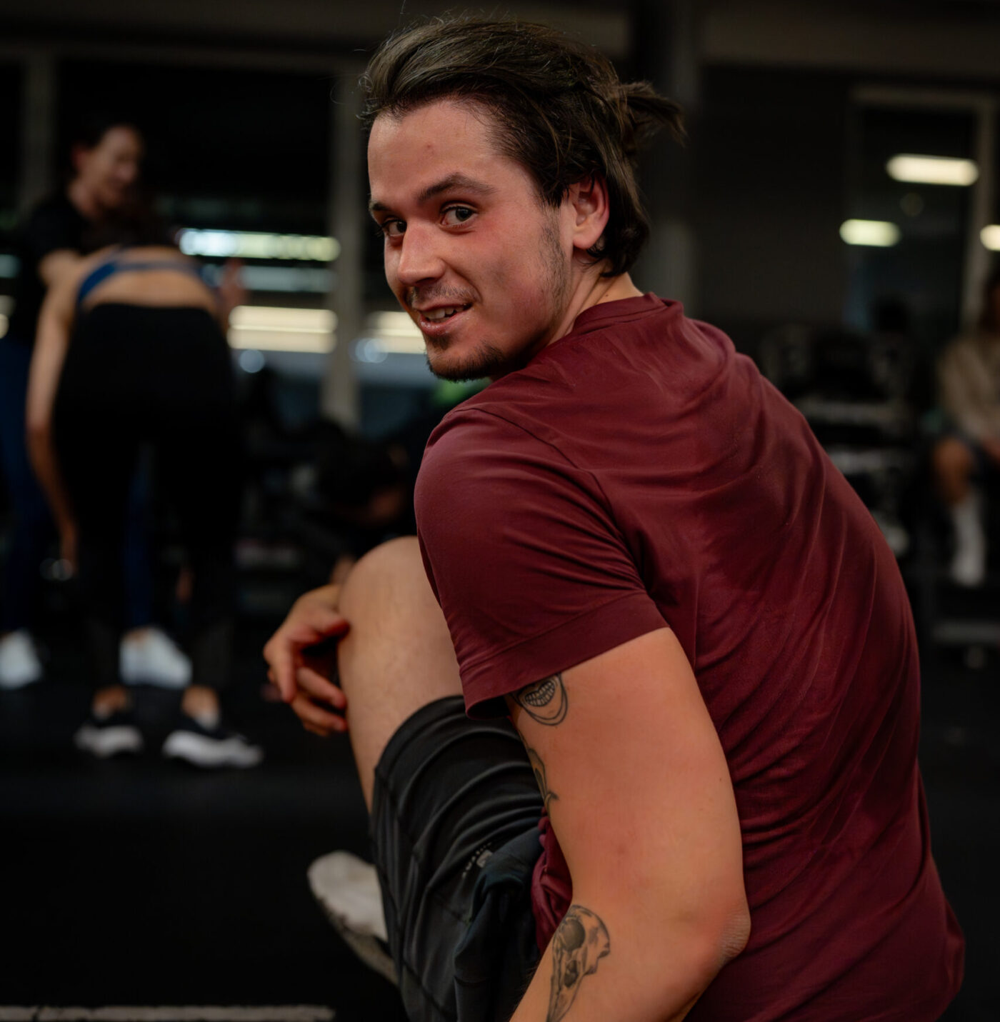 Uśmiechnięty młody mężczyzna w bordowej koszulce sportowej podczas treningu na siłowni Well Fitness.