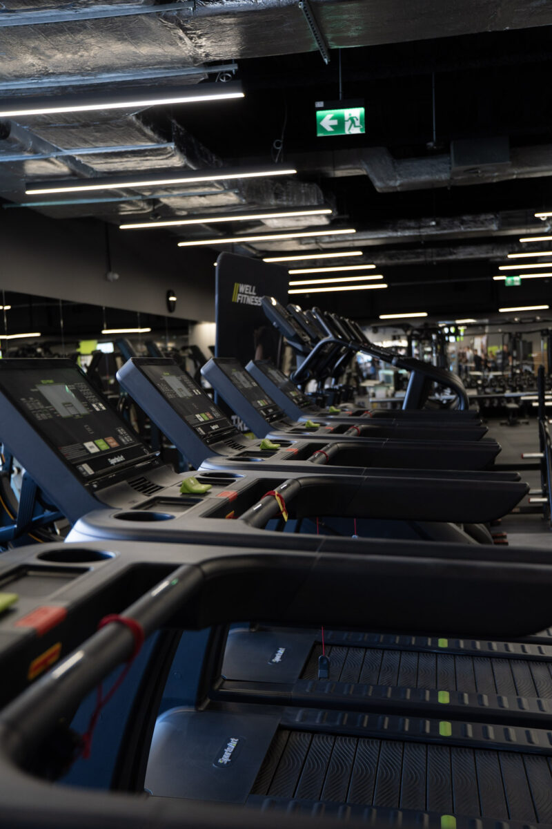 A perspective of a row of cardio machines by Matrix, showing the rhythmic arrangement of black handles against an industrial, dark ceiling with linear lighting.