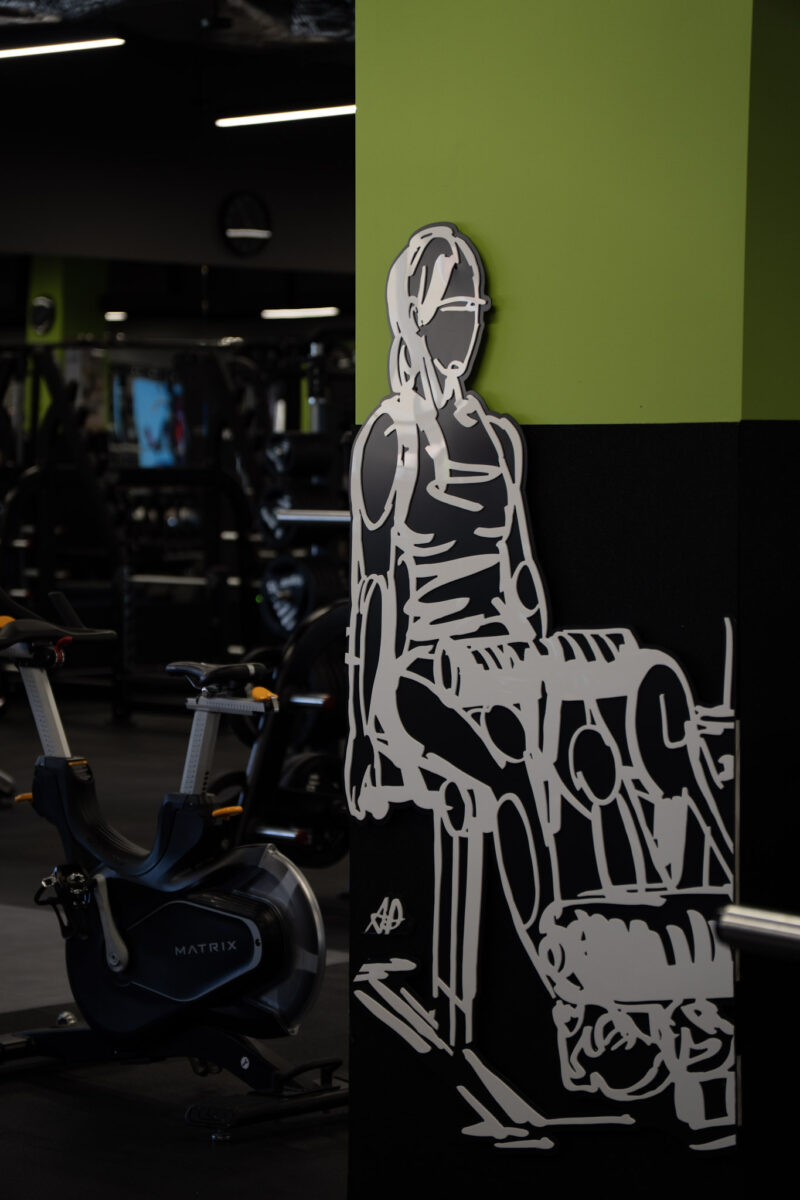 A wall-mounted decorative graphic depicting the silhouette of a person exercising on a machine, placed next to a Matrix stationary exercise bike.