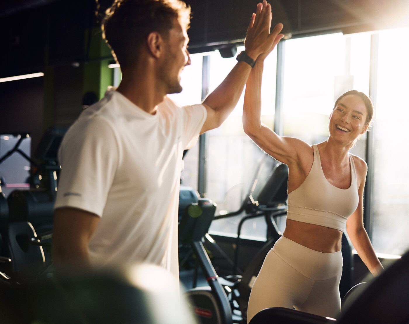 Mężczyzna i uśmiechnięta kobieta przybijają piątkę podczas treningu na siłowni Well Fitness.